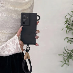 Person holding a black phone case with a lanyard on a light background